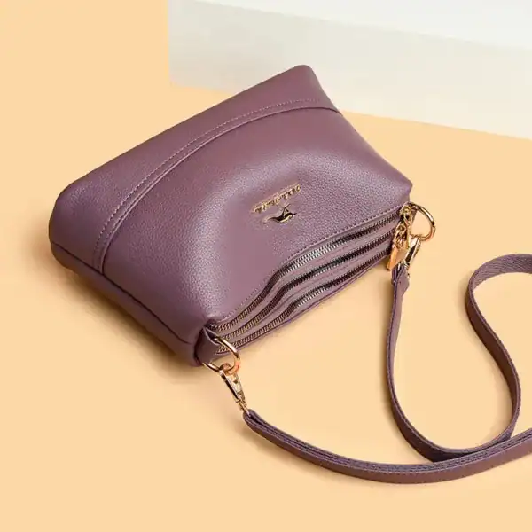 Cognac liten crossbody axelväska i lila läder med dubbel dragkedja och axelrem.