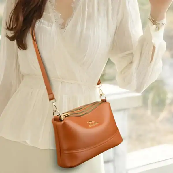 Cognac färgad liten crossbody axelväska med guld detaljer och läderrem.