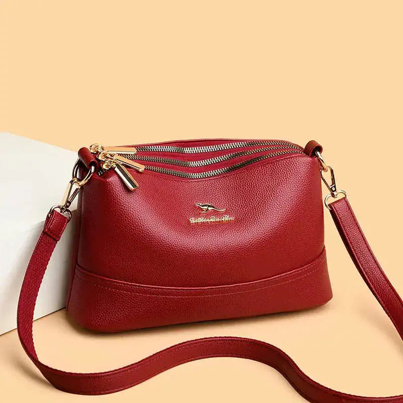 Rött läder crossbody väska med guld dragkedja och axelrem.