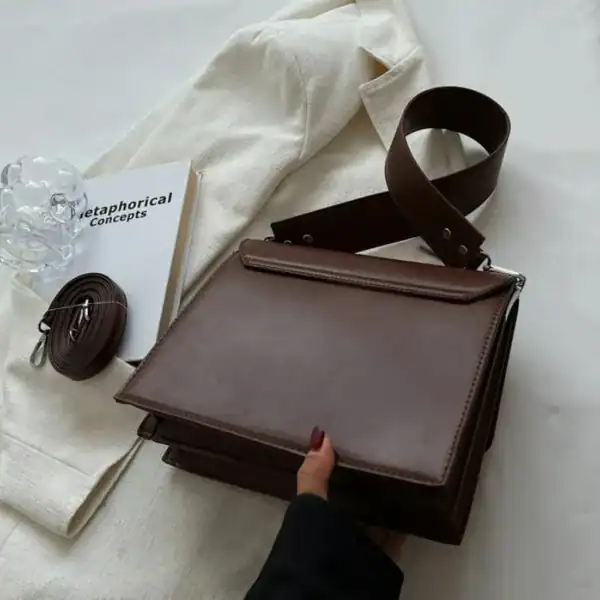 Cognac färgad axelväska med lock, läder, minimalistisk design, handtag och axelrem.