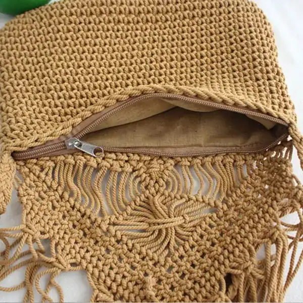 Flätad handväska i beige med fransar och dragkedja.