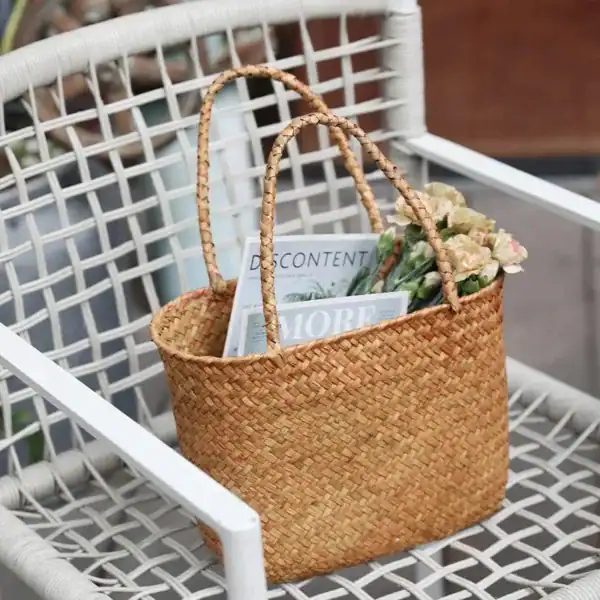 Flätad korgväska beige med blommor och tidningar på utomhusstol.