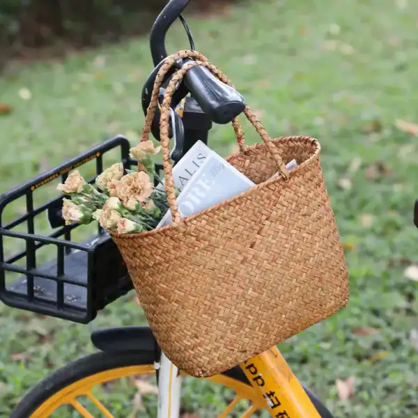 Flätad korgväska beige på cykel, med blommor och tidning.