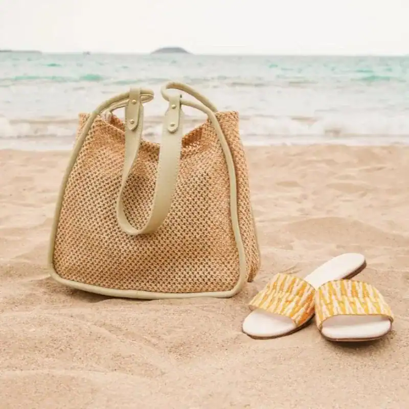 Beige flätad shoppingväska på stranden med sandaler.