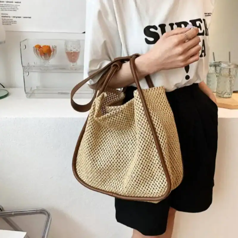Beige flätad shoppingväska med brun läderhandtag, trendig och lätt att bära.