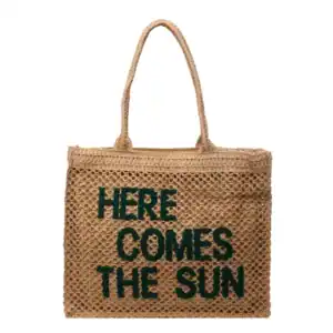 Flätad väska med text 'HERE COMES THE SUN', trendiga sommarväskor.