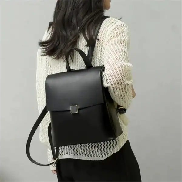 Svart ryggsäck med metallficka, bärt av kvinna i vit tröja.
