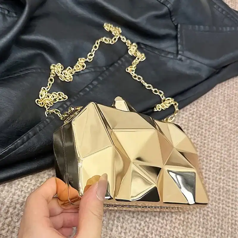 Guldig geometrisk clutch med kedjehandtag och metallisk yta.
