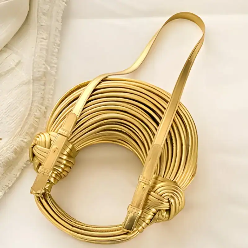Guldig knuten väska, elegant guldfärgad axelväska med knutdetaljer och läderrem.