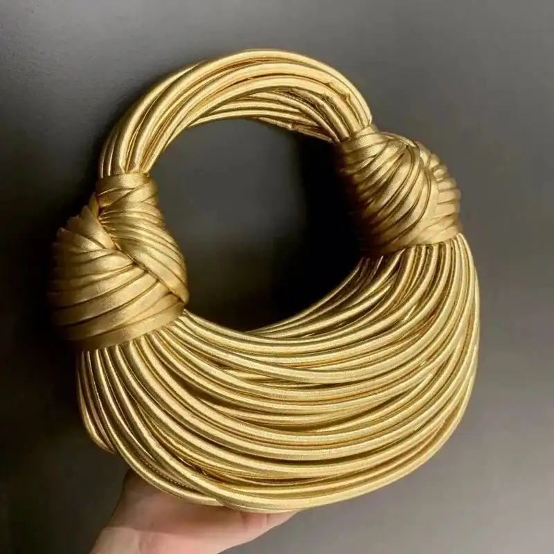Guldig knuten väska med elegant snörad handtag och glittrande guldton.