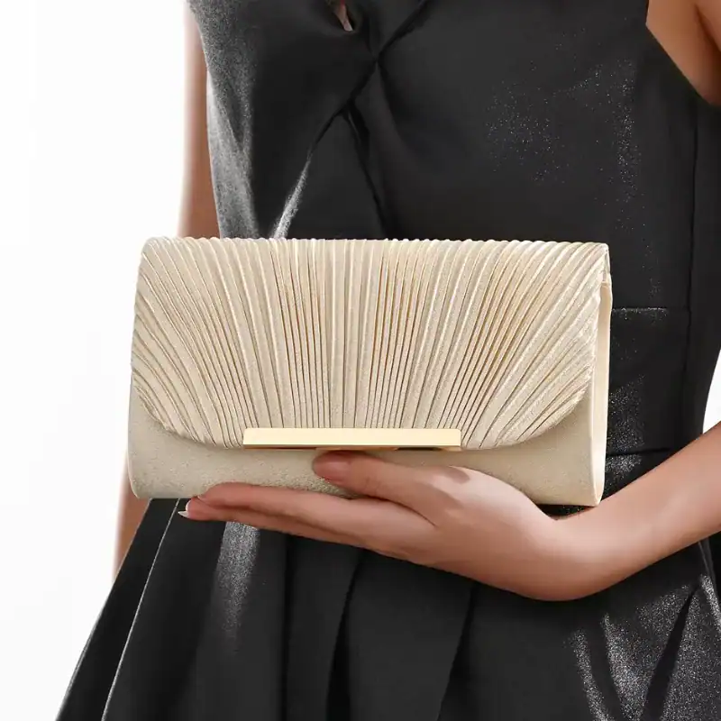 Guldig plisserad clutch i cremefärg, hållen av en kvinna i svart klänning.
