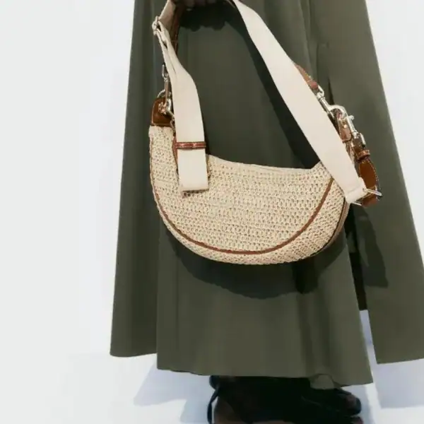 Halvmånsväska i strå med beige axelrem och bruna läderdetaljer.