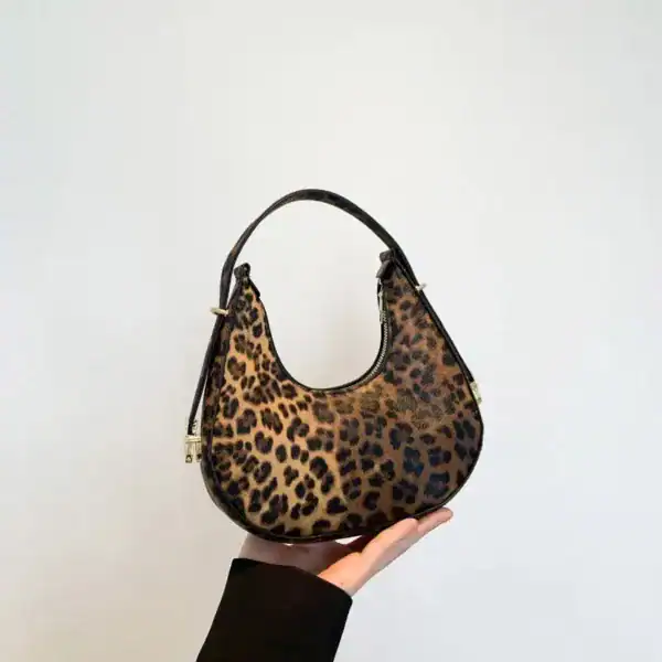 Hoboväska med leopardmönster, hålls i handen mot vit bakgrund.