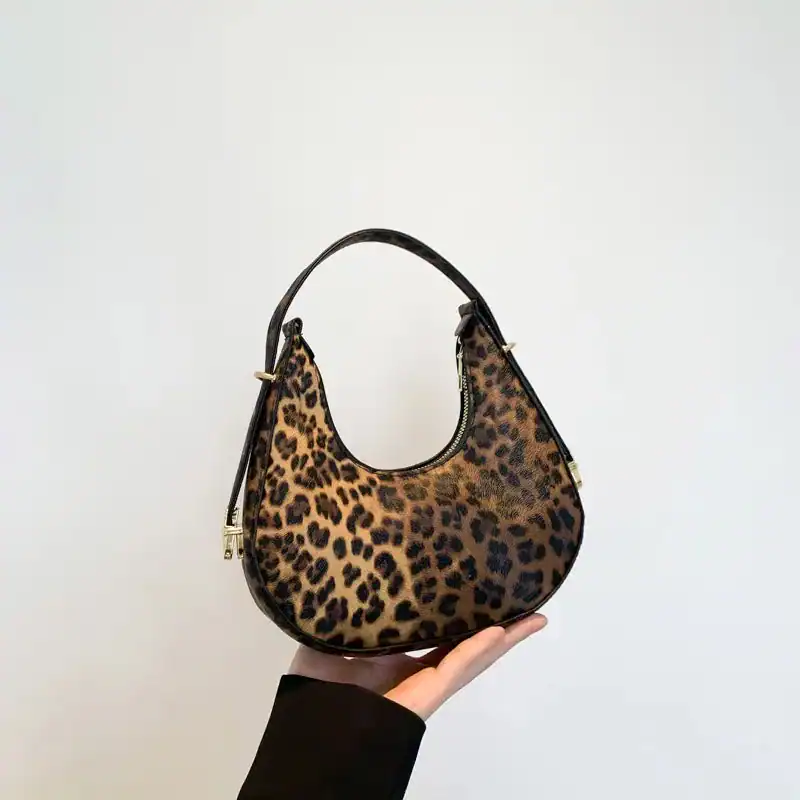 Hoboväska med leopardmönster, hålls i handen mot vit bakgrund.