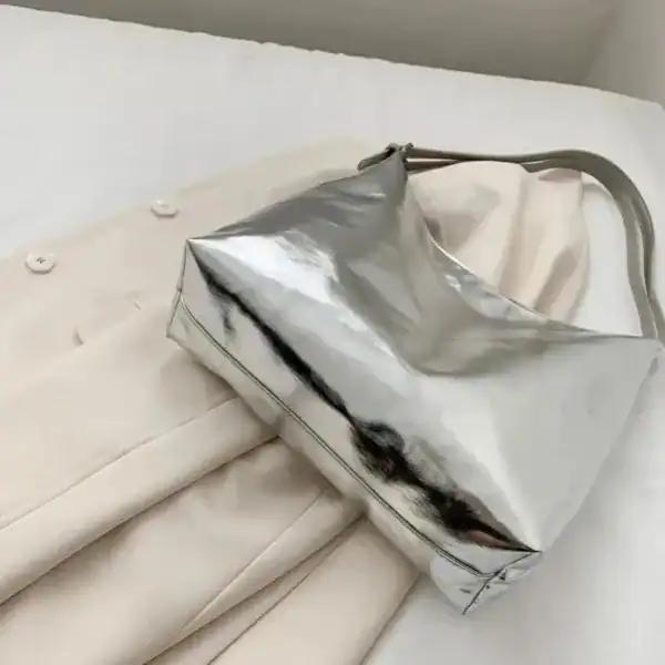 Silver hobo handväska med glansig yta, placerad på beige kläder.