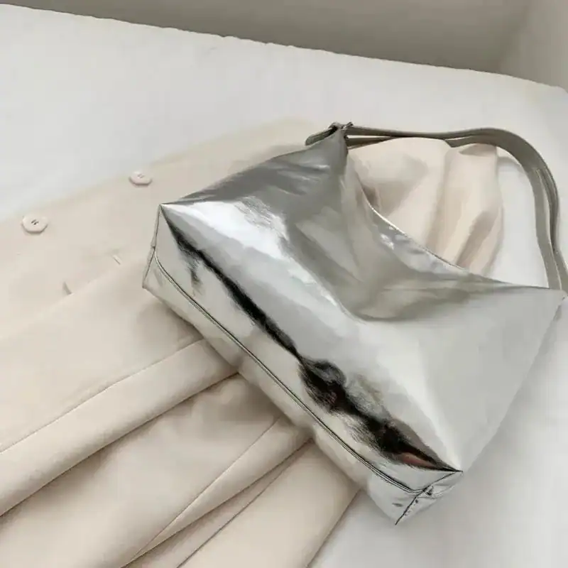 Silver hobo handväska med glansig yta, placerad på beige kläder.