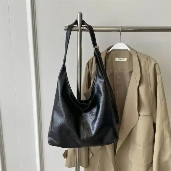 Svart hobo väska i läder, hängande på klädstång bredvid beige jacka.