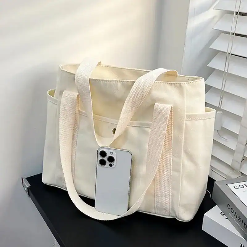 Krämvit canvas shoppingväska med mobil i axeln, stilren och praktisk för daglig användning.