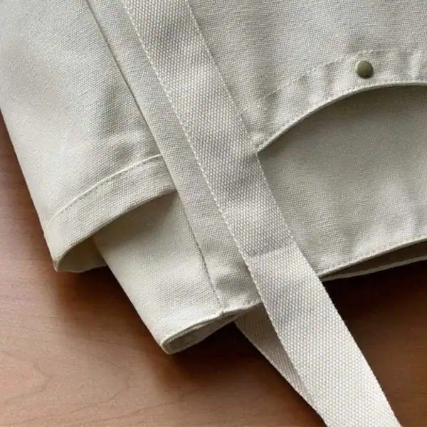 Krämvit canvas shoppingväska med robusta handtag och detaljerad sömmar.