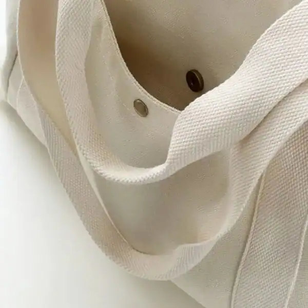 Krämvit canvas shoppingväska med robusta handtag och metallögon.