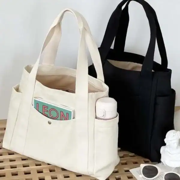 Krämvit canvas shoppingväska med fickor och vattenflaska.