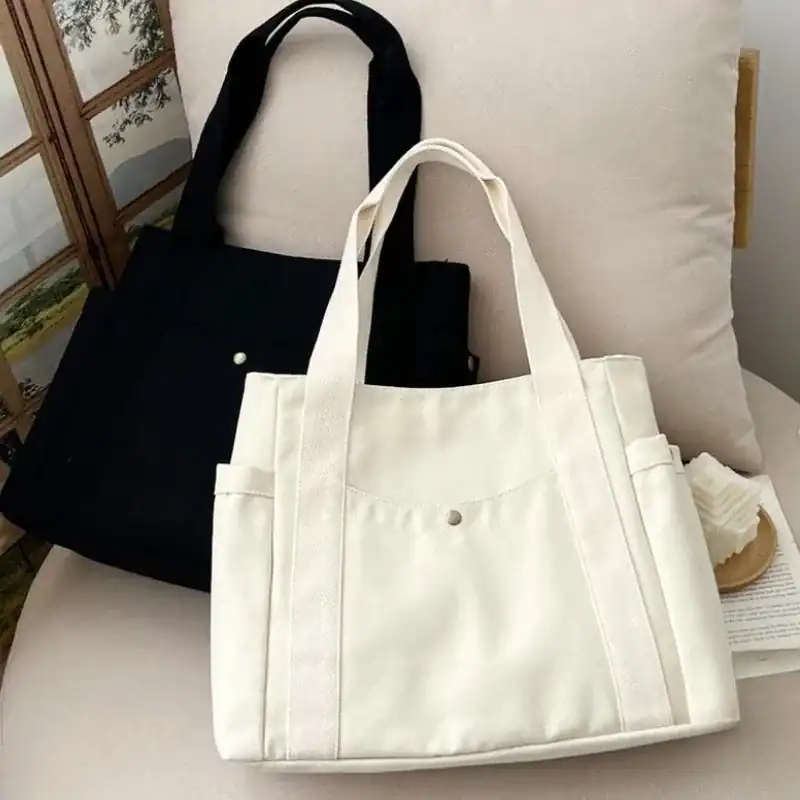 Krämvit canvas shoppingväska med platt framsida och handtag, ideal för daglig användning och shopping.
