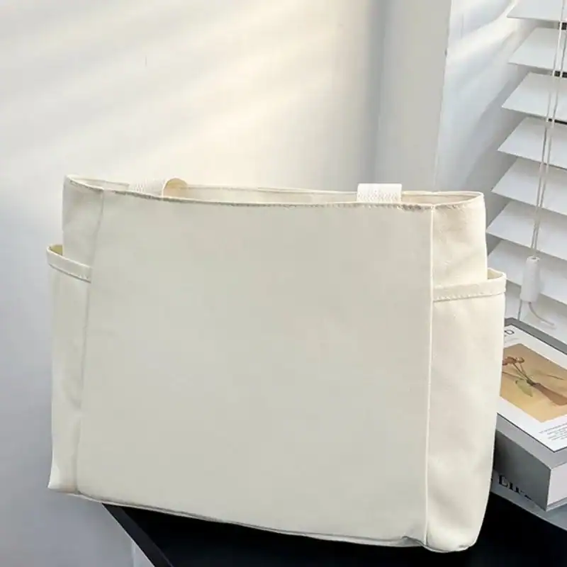 Krämvit canvas shoppingväska med sidopåsar och minimalistisk design.