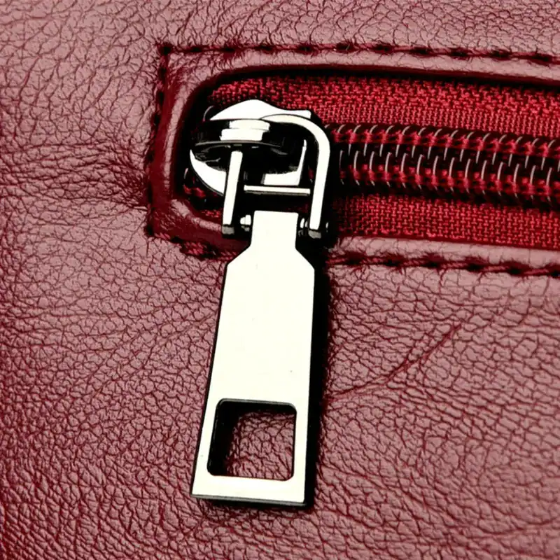 Krämvit crossbody väska med metallisk dragkedja och röd läderliknande yta.