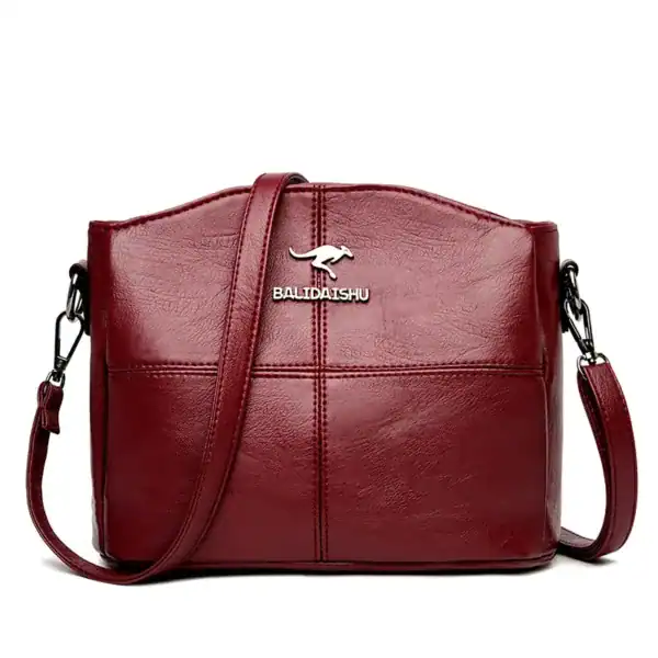 Krämvit crossbody väska med metalldetalj och läderliknande yta.