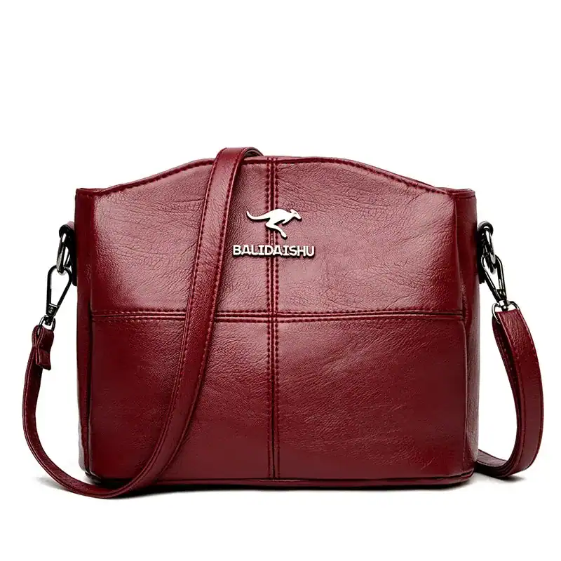 Krämvit crossbody väska med metalldetalj och läderliknande yta.