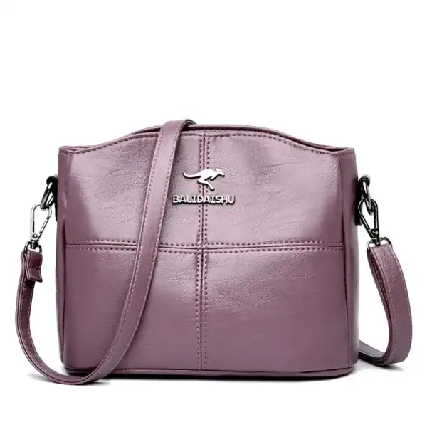 Krämvit crossbody väska med metalliskt logo och justerbar axelrem.