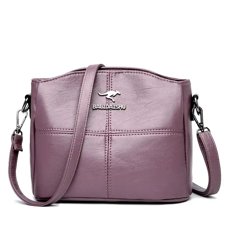 Krämvit crossbody väska med metalliskt logo och justerbar axelrem.