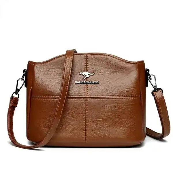 Krämvit crossbody väska med metalldetalj och läderliknande yta.