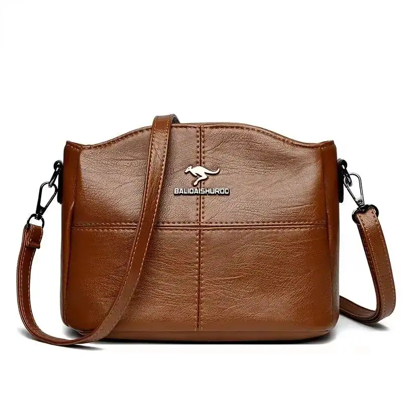 Krämvit crossbody väska med metalldetalj och läderliknande yta.
