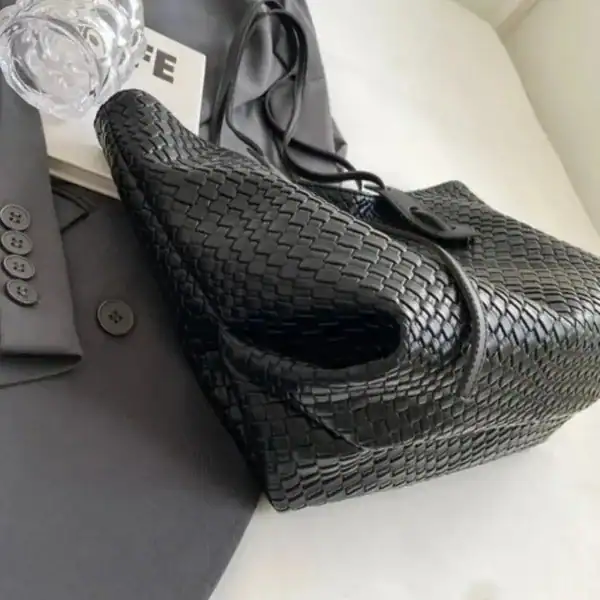 Krämvit flätad shoppingväska i svart, elegant design med handtag och öppen topp.