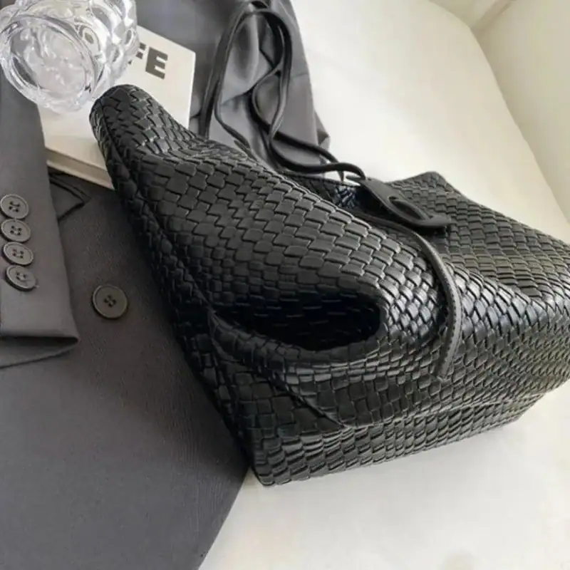 Krämvit flätad shoppingväska i svart, elegant design med handtag och öppen topp.