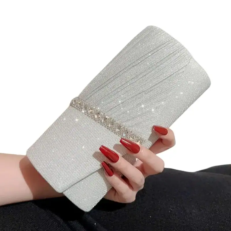 Krämvit glitterclutch med kristallbesättningsband och röd nagellack.