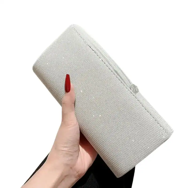 Krämvit glitterclutch i hand, elegant och perfekt för festliga tillfällen.