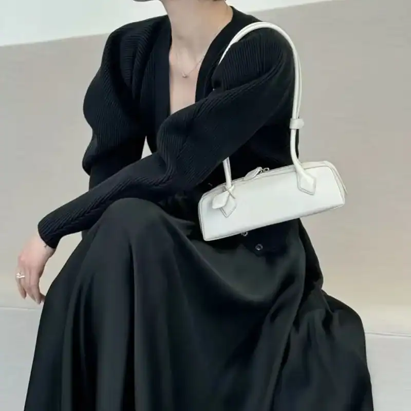 Krämvit handväska i minimalistisk stil, bäras av kvinna i svart klänning och cardigan.