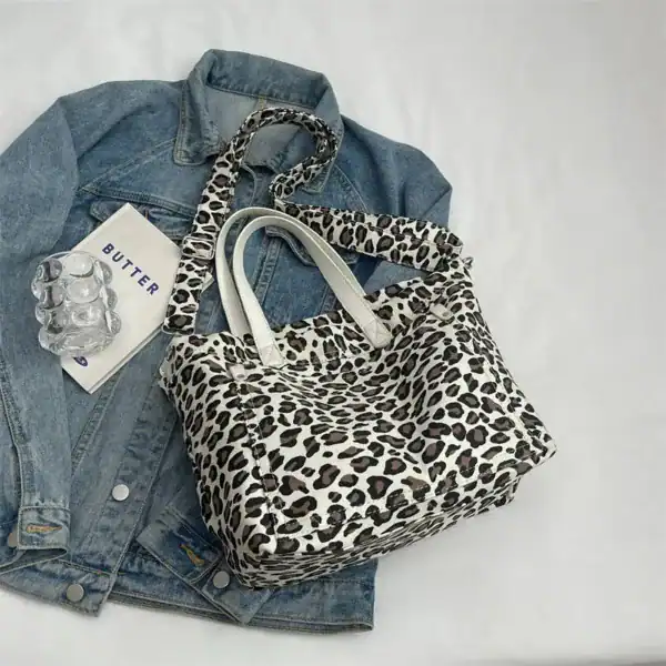 Leopard mönster axelväska med vitt handtag, placerad på jeansjacka.