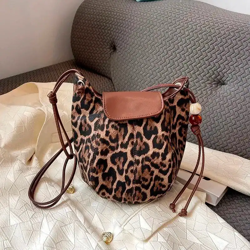 Leopard halvmånsväska med brun läderlock och pärlor på axelremmen.
