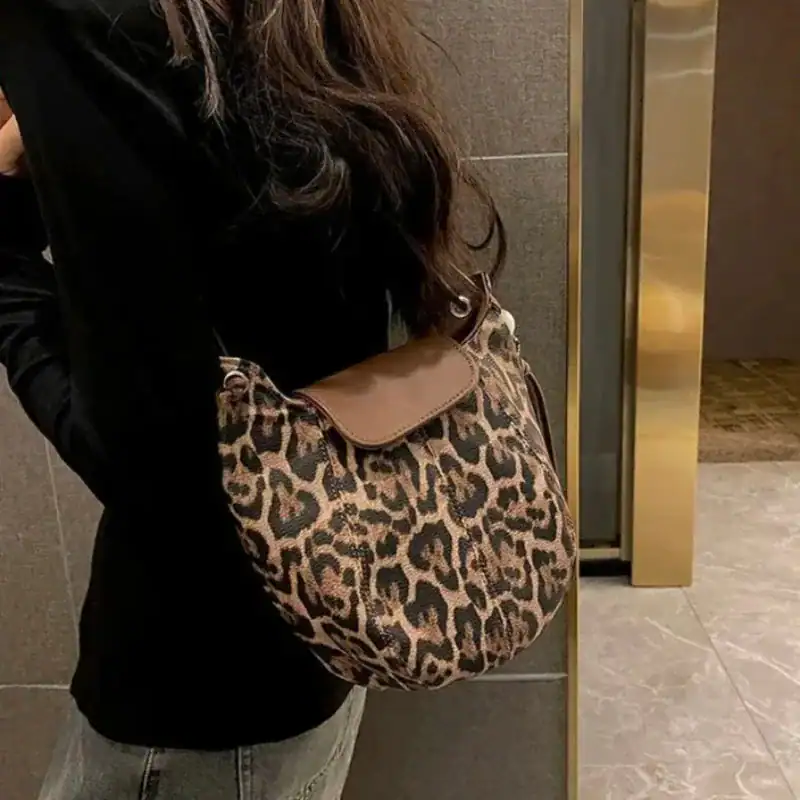 Leopard halvmånsväska i beige och svart, bäras av kvinna i svart tröja.