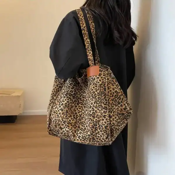 Leopard mökkaväska i beige och svart, bäras över axeln av en kvinna i svart klädsel.