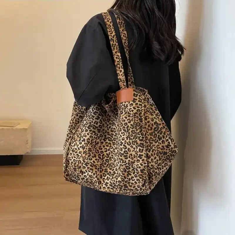 Leopard mökkaväska i beige och svart, bäras över axeln av en kvinna i svart klädsel.