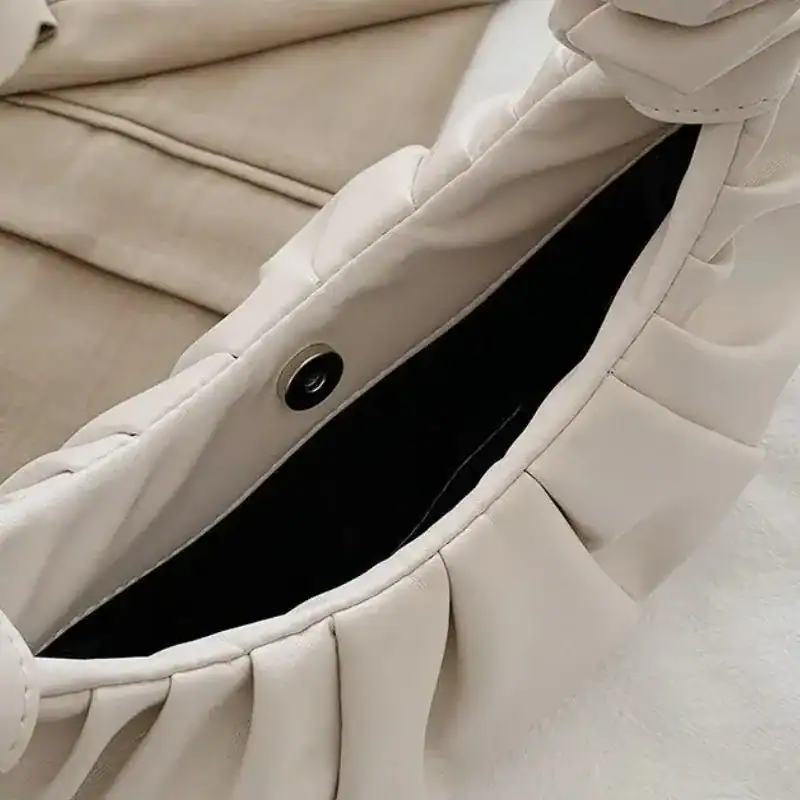 Beige plisserad väska med svart inre och metallknapp.