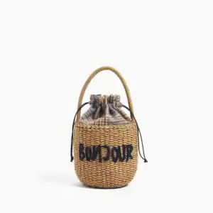 Liten stråväska med text 'BONJOUR', dragsnörd, handtag, sommarväska.