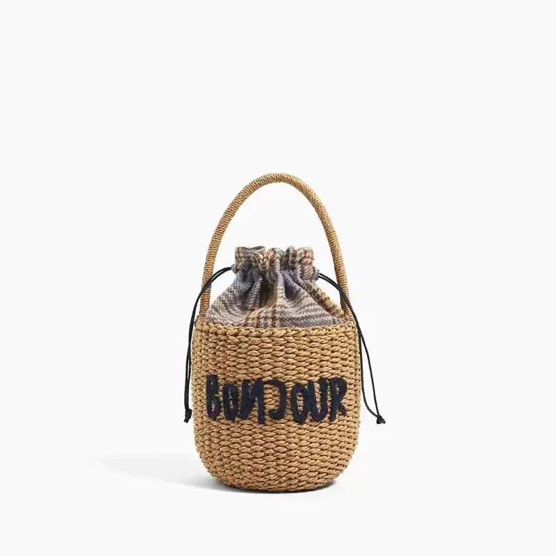 Liten stråväska med text 'BONJOUR', dragsnörd, handtag, sommarväska.