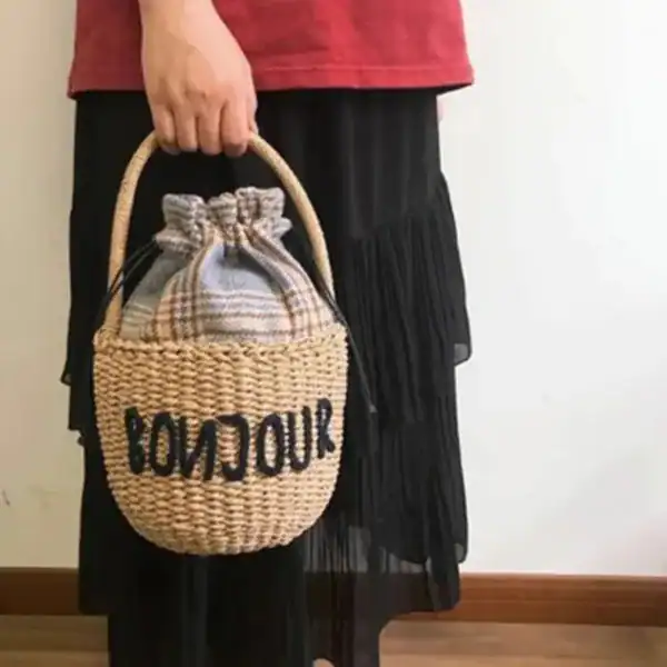 Liten stråväska med text 'BONJOUR', handtag, plädinnehåll.