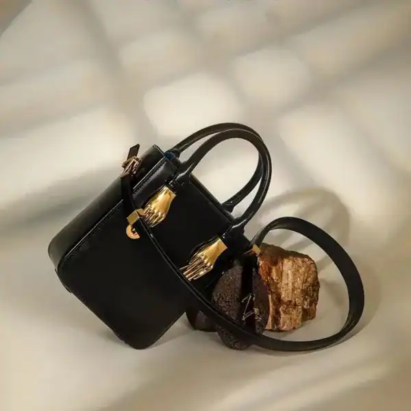Liten svart shoppingväska med guldhandtag, elegant och trendig för vardag och fest.