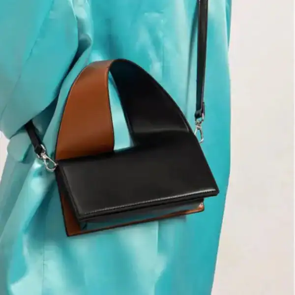 Liten svart väska med brunt handtag och axelrem, modern design.